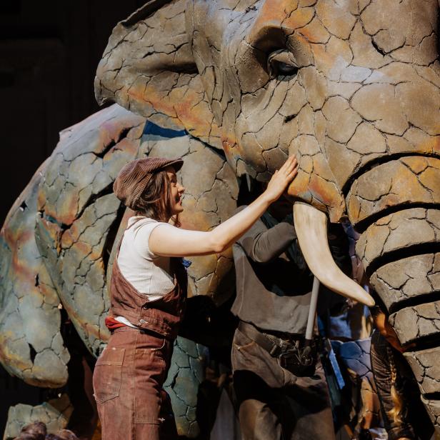 Eine Frau berührt den Kopf eines großen, skulpturartigen Elefanten.