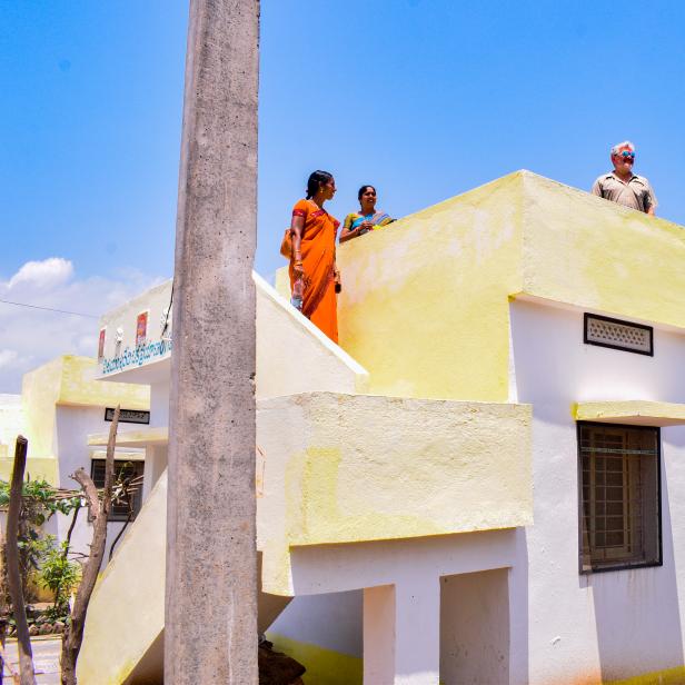 Zwei Frauen in Saris und ein Mann stehen auf dem Dach eines Hauses.