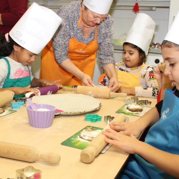 Kinder backen mit einer älteren Frau in einer Küche Kekse.