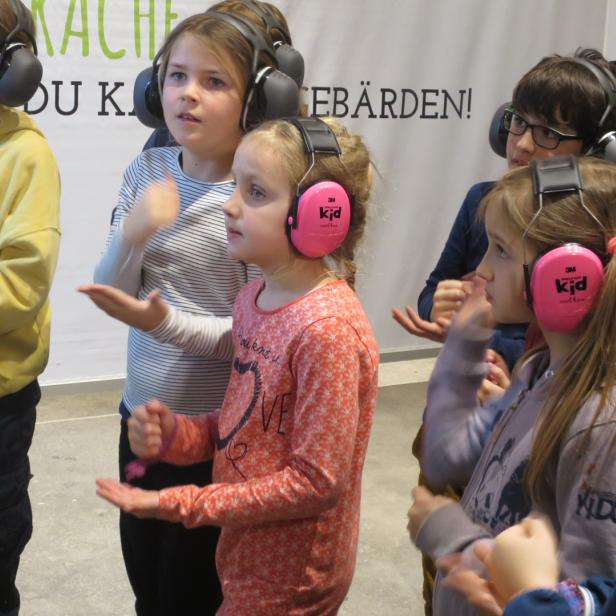 Eine Gruppe Kinder mit Kopfhörern lernt Gebärdensprache.