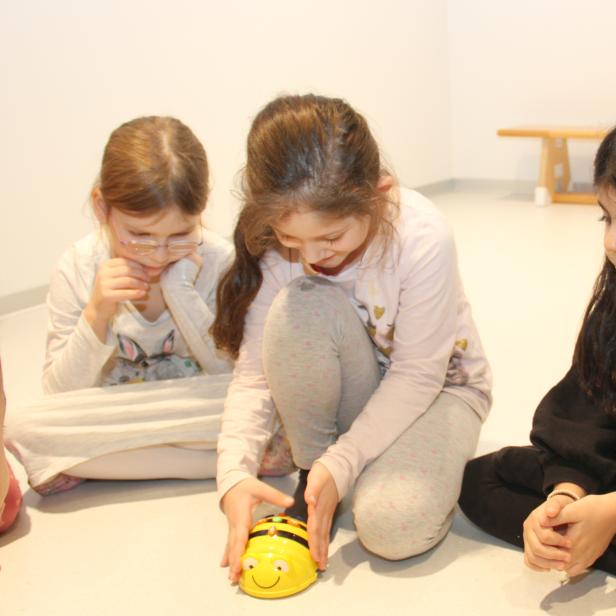 Eine Gruppe Kinder sitzt auf dem Boden und spielt mit einem gelben Spielzeugroboter.