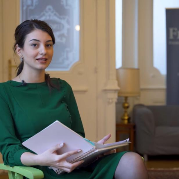Eine Frau in einem grünen Kleid sitzt mit einem Notizbuch in einem Raum.