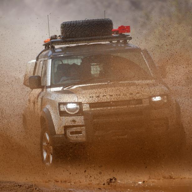 Ein Land Rover Defender fährt durch eine schlammige Wasserstelle.