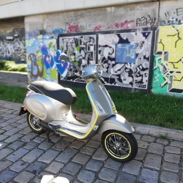 Eine silberne Vespa steht vor einer Wand mit Graffiti.