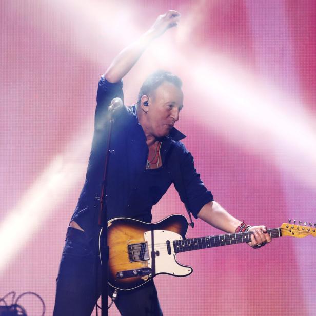 Bruce Springsteen spielt Gitarre auf einer Bühne mit rosa Lichteffekten.