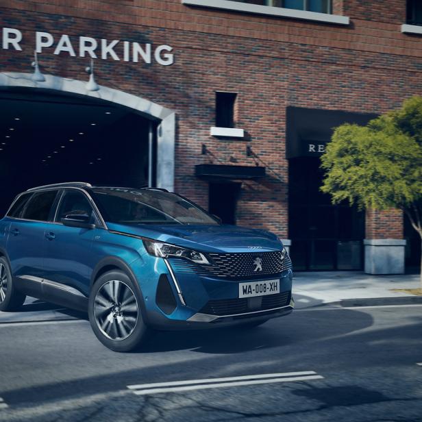 Ein blauer Peugeot 3008 parkt vor einem Gebäude mit der Aufschrift „Visitor Parking“.