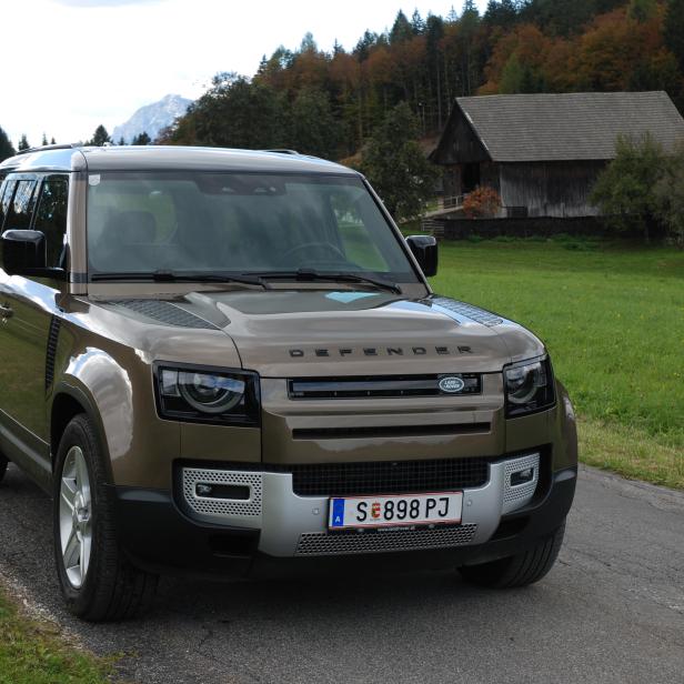 Ein brauner Land Rover Defender steht auf einer Straße in ländlicher Umgebung.