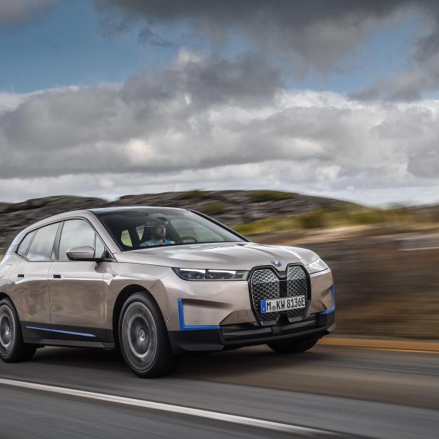 Ein goldfarbener BMW iX fährt auf einer Landstraße.