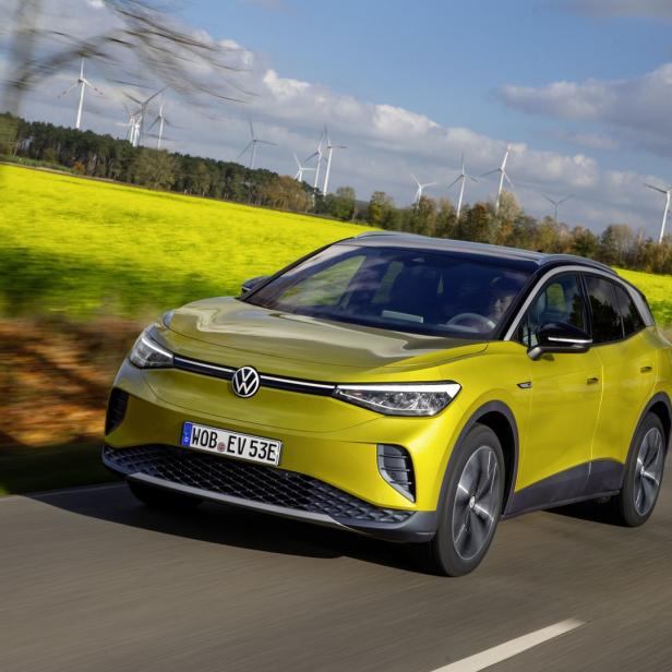 Ein gelber VW ID.4 fährt auf einer Straße, im Hintergrund Windräder und ein Rapsfeld.