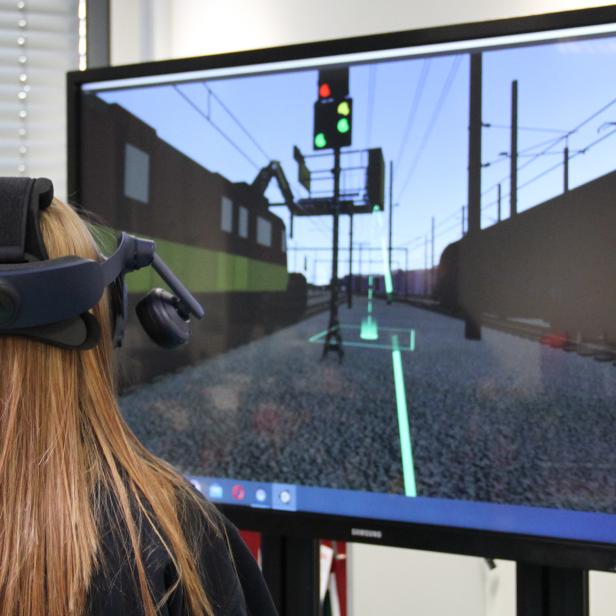 Jugendliche mit VR-Brille vor Monitor mit Bahnanlage.