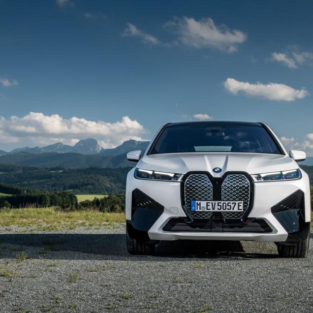 Ein weißer BMW iX steht vor einer Berglandschaft.