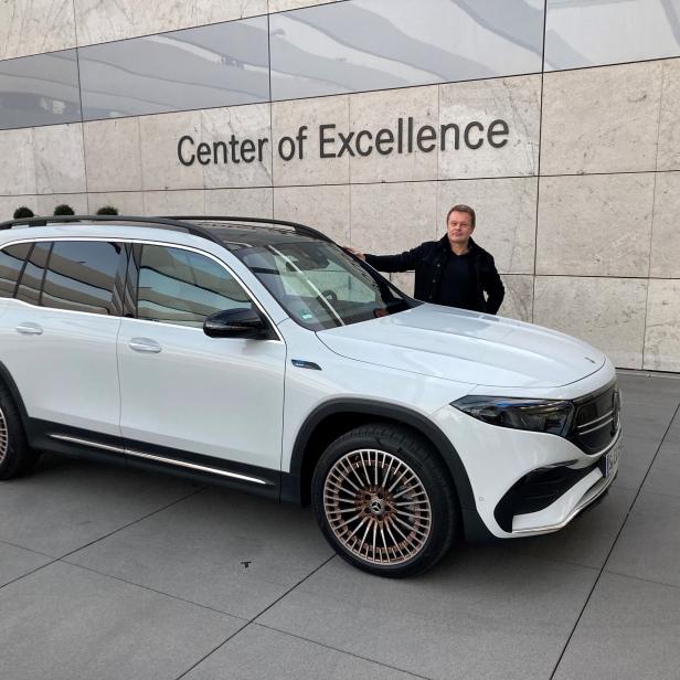 Ein Mann posiert neben einem weißen Mercedes-Benz EQA vor dem „Center of Excellence“.