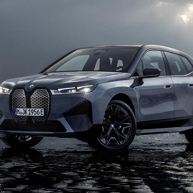 Ein grauer BMW iX steht am Strand unter einem bewölkten Himmel.