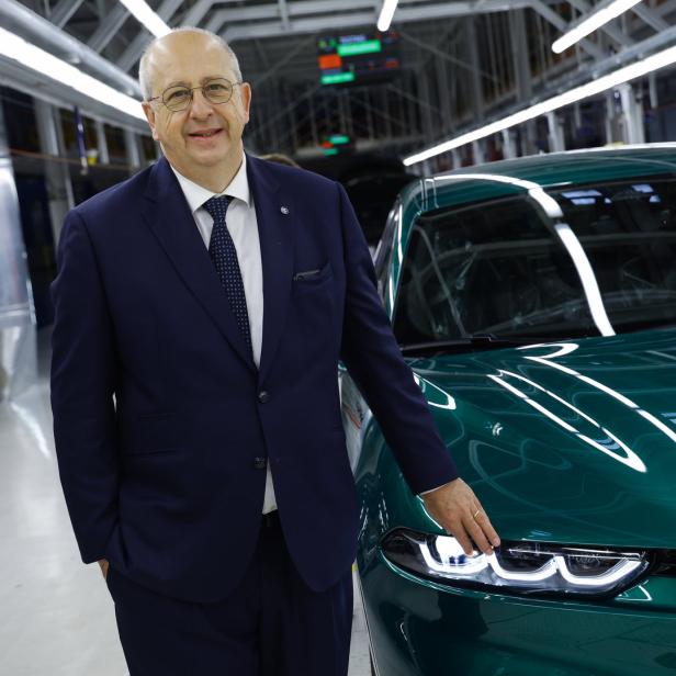 Ein Mann im Anzug posiert neben einem grünen Alfa Romeo in einer Fabrikhalle.