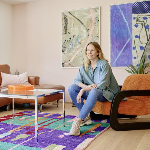 Eine Frau sitzt in einem Sessel in einem Wohnzimmer mit farbenfrohem Teppich.