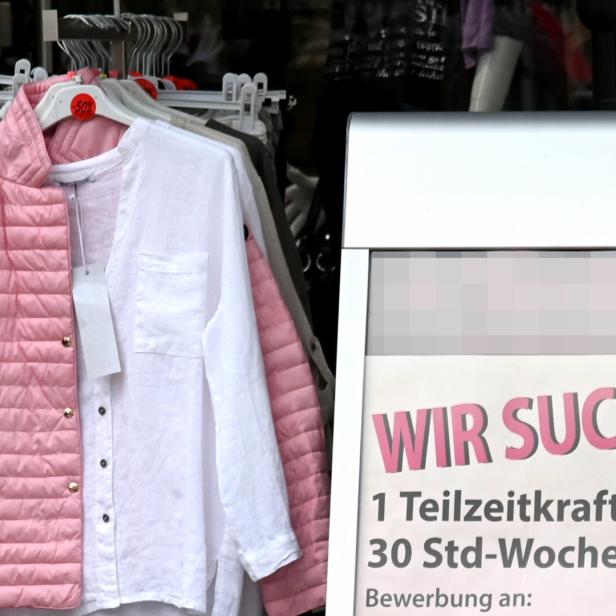 Eine rosa Steppjacke und ein weißes Hemd hängen vor einem Geschäft, das eine Teilzeitkraft sucht.