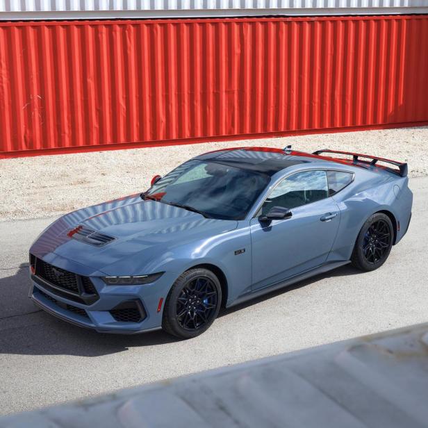 Ein blauer Ford Mustang Mach-E steht vor roten und weißen Containern.