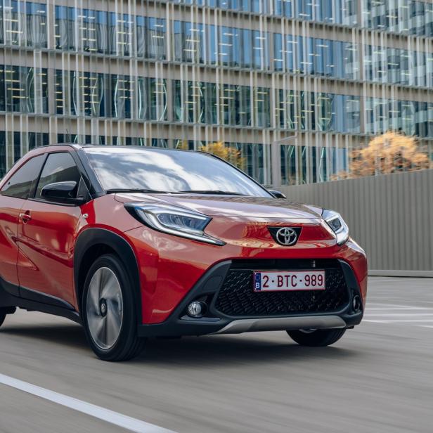 Ein roter Toyota Aygo X fährt vor einem modernen Bürogebäude.