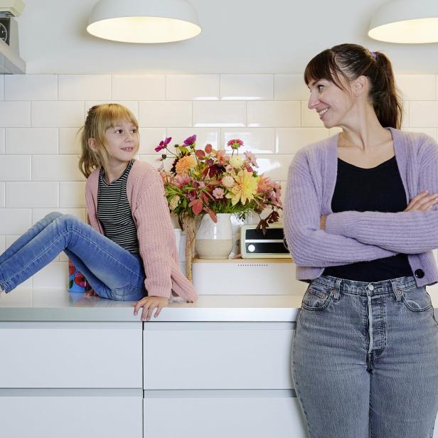 Ein Mädchen sitzt auf der Küchentheke, während eine Frau daneben steht und sie anlächelt.