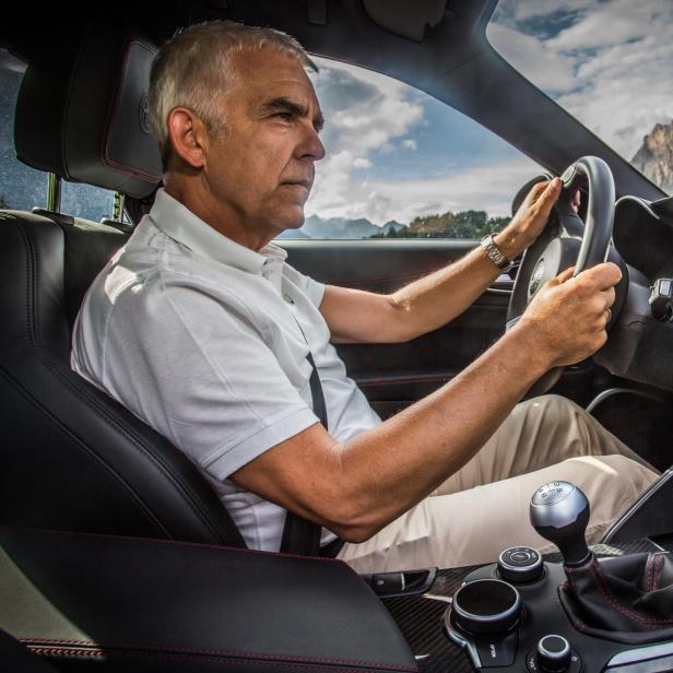 Ein Mann fährt ein Auto mit Bergkulisse im Hintergrund.