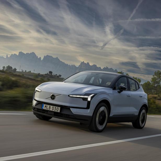 Ein hellblauer Volvo EX30 fährt auf einer Landstraße vor einer Bergkulisse.