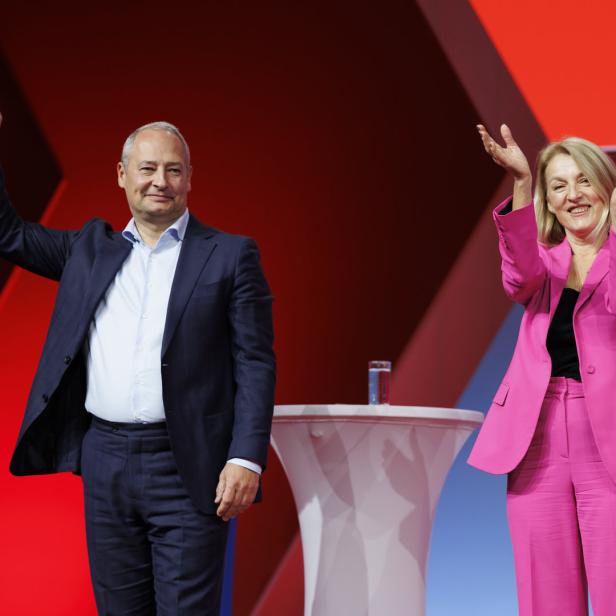 Ein Mann im Anzug und eine Frau im pinkfarbenen Hosenanzug winken auf einer Bühne.