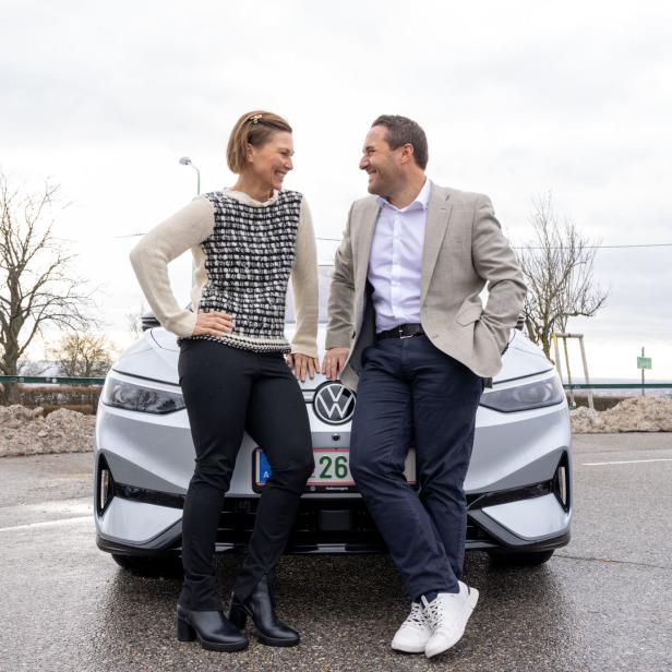 Eine Frau und ein Mann stehen vor einem silbernen Volkswagen ID.4 und unterhalten sich.